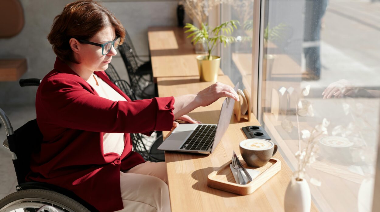 Jeune femme sur son fauteuil rulant placé devant un bureau où est placé un ordinateur portable sur lequelle elle semble travailler.